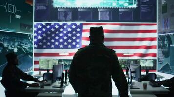 US army official working on ensuring servers protection and state secrets, protecting important hybrid warfare data in high tech agency office. Military soldier supervises hacking activity. Camera B. video