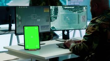 Soldier gathering real time surveillance data next to mockup display in high tech command center, processing intelligence for field operations. Working with modern gear and big screen. Camera A. video