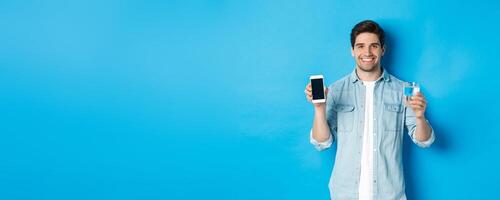 Young man control water balance with smartphone app, showing mobile screen app and smiling, standing over blue background photo