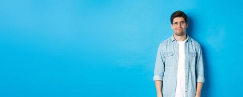 Skeptical and doubtful guy in glasses, looking confused at something strange, blue background photo