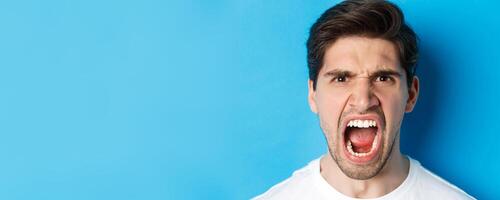 Head shot of angry man shouting and looking with hatred, standing mad against blue background photo