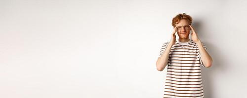 Handsome young man with hipster red hairstyle and glasses, smiling at camera, standing over white background photo
