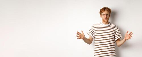 Impressed redhead man in glasses showing length of something big, demonstrate large size and looking amazed, standing over white background photo