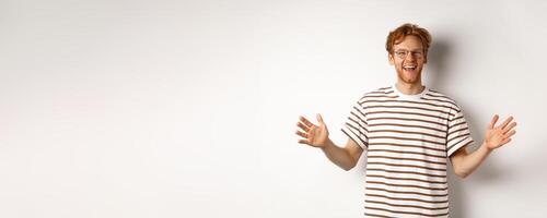 Attractive young man with red hair and glasses showing large size, length of big object, smiling satisfied, standing over white background photo