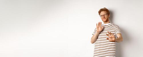 Displeased young man with red hair and bristle showing stop gesture, refusing something bad with disgusted face, standing over white background photo