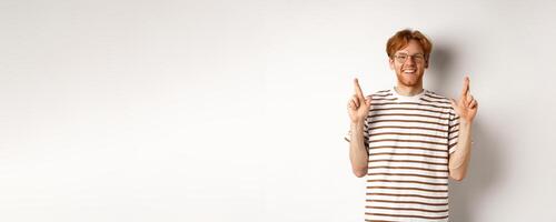 Hopeful and optimistic man with ginger hair and glasses having hope, making wish and cross fingers for good luck, smiling at camera, white background photo