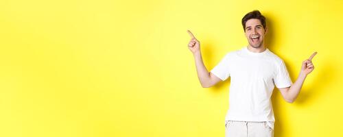 Happy stylish guy showing two variants, pointing fingers sideways at left and right promo, standing over yellow background photo