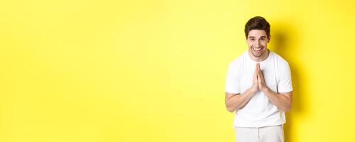 Handsome guy saying thank you, bowing and holding hands in namaste gesture, express gratitude, standing over yellow background photo