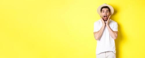 Concept of tourism and summer. Surprised male model in straw hat, looking amazed at special offer, standing against yellow background photo