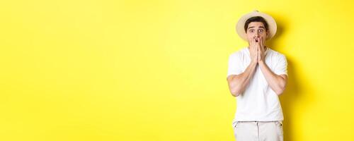 Concept of tourism and summer. Shocked guy jumping from fear, standing startled against yellow background photo