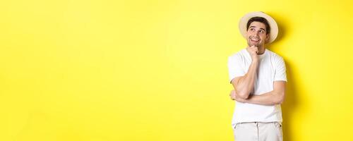 Young thoughtful man tourist imaging something, looking at upper left corner and smiling, thinking and standing over yellow background photo