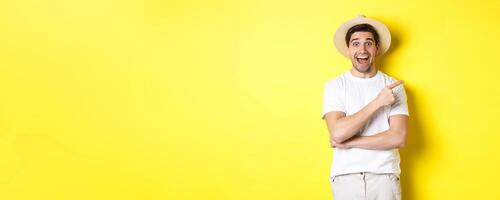 Happy male tourist in straw hat pointing finger right, showing promo offer on copy space, yellow background photo