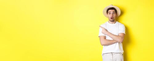 Concept of tourism and lifestyle. Surprised handsome man tourist pointing finger left, looking impressed about promo offer, yellow background photo