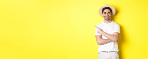 Concept of tourism and lifestyle. Young man tourist pointing finger left, looking happy, showing special holidays promo, yellow background photo