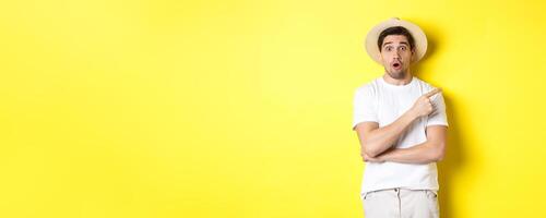 Surprised man in straw hat pointing finger right, showing promo banner, standing over yellow background photo