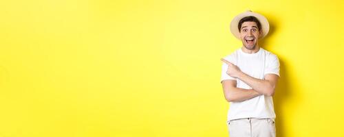 Concept of tourism and lifestyle. Happy young male tourist showing advertisement, pointing finger left and smiling excited, yellow background photo