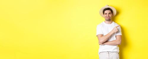 Skeptical male tourist complaining, pointing finger right at something bad or lame, standing unamused against yellow background photo