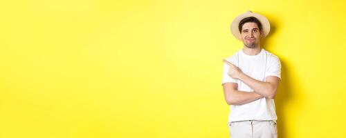 Concept of tourism and lifestyle. Skeptical guy tourist complaining, pointing finger left at something bad, looking displeased, yellow background photo