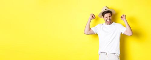 Concept of tourism and vacation. Happy man rejoicing, winning something or achieve goal, triumphing against yellow background photo