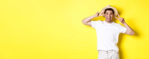 Concept of tourism and vacation. Happy man tourist posing for photo with peace signs, smiling excited, standing against yellow background