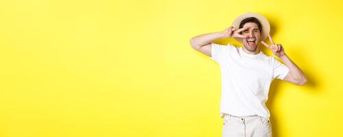 Concept of tourism and vacation. Happy man tourist posing for photo with peace signs, smiling excited, standing against yellow background