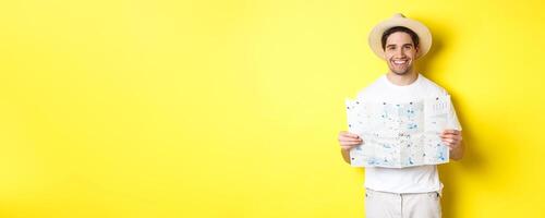 Travelling, vacation and tourism concept. Smiling young man going on trip, holding road map and smiling, standing over yellow background photo