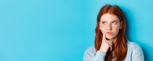 Headshot of troubled teenage girl thinking, looking bothered and frowning, standing against blue background photo