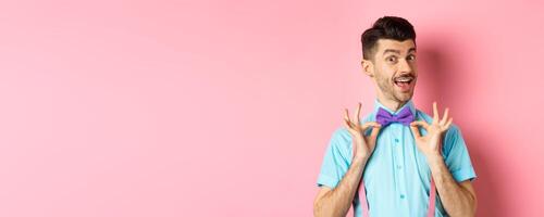 Classy handsome man fixing bow-tie on neck and smiling, getting ready for date or party, standing on pink background photo