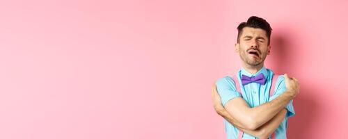 Crying guy hugging himself, feeling sad and lonely, standing unhappy on pink background photo