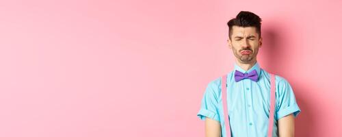 Sad and lonely man crying on valentines day, feeling lonely without lover, standing over pink background photo