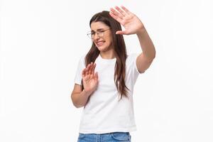 No please dont hurt me. Portrait of reluctant and disstressed, young disgusted woman pulling hands in defense, trying protect herself and step back turn away from glimmering light, grimacing photo