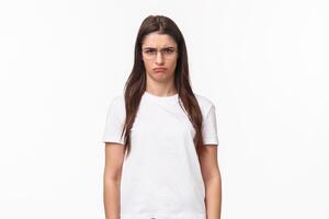 Waist-up portrait of sulking young offended gloomy girl, look with contempt camera, squinting blame person for spoiling her holiday, frowning grumpy, standing white background photo
