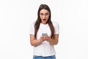 Communication, technology and lifestyle concept. Portrait of surprised and amazed, excited young caucasian woman in glasses, looking at mobile phone, receive awesome new via text message photo