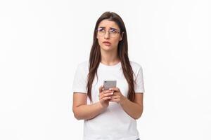 Communication, technology and lifestyle concept. Portrait of troubled and concerned young woman worried for friend, sending text message if shes okay and thinking, look up nervous, hold mobile phone photo
