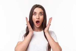 What an amazing news. Surprised and astonished, excited young woman react to something awesome happened, gasping, open mouth and raise hands near face, staring camera, white background photo