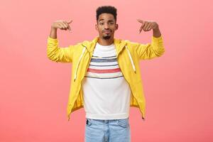 How you like my style. Cool and handsome stylish young man with beard in trendy yellow jacket over t-shirt raising hands pointing at himself smirking and raising eyebrow being unsure how he looks photo