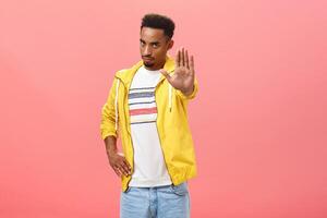 Hold on not move. Portrait of serious-looking intense handsome dark-skinned guy in trendy outfit pulling palm in warn gesture, demanding to stop or obey rules over pink background photo