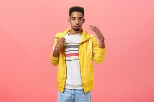 Guy dressed up unappropriatly for hot weather sweating breathing out and making wind with shook palm to cool down pulling collar of t-shirt while feeling discomfort walking on street in warm jacket photo