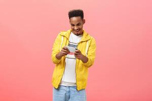 Enthusiastic guy having fun playing awesome smartphone game holding cellphone in both hands staring at device screen with passion and thrill spending free time in internet over pink background photo