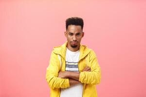 Displeased offended attractive african american male with beard and curly hairstyle frowning holding hands crossed pouting ready to cry, whining being silly and childish over pink wall photo