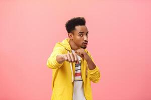 Guy acting cool bragging in front of girlfriend with mascules showing boxer moves standing in boxing pose with raised fist in punch gesture turning right as if fighting over pink background photo