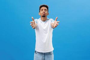 Come and give me kiss. Portrait of passionate romantic and pleased african american guy with beard pulling hands towards camera and folding lips in mwah wanting cuddle, expressing affection photo
