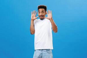 Man feeling awkwards and shocked seeing naked friend trying cover eyes with raised palms screaming from shook raising eyebrows astonished and stunned bending backwards terrified over blue wall photo
