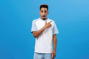 Man feeling shocked finding out friend betrayed him pointing at upper right corner frowning and opening mouth with concerned upset and unhappy expression posing over blue background worried photo