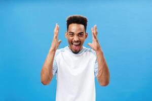 Waist-up shot of man going furious being in rage shouting and yelling from anger stressing out and arguing with girlfriend having fight shaking raised arms standing over blue background photo