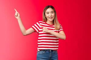 Enthusiastic friendly modern asian blond girl suggest perfect place hang promo pointing upper left corner smiling look camera assertive introduce project, recommend link, stand red background photo
