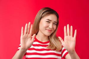 No thanks I pass. Reluctant lazy cute asian modern girl show hands block rejection gesture, smirking displeased shake head no emotion, unwilling participate, show refusal, stand red background photo