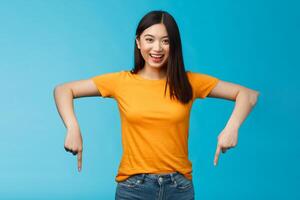 Enthusiastic pleasant asian blong modern female student inviting you visit awesome event pointing down indicating bottom advertisement, stand blue background smiling broadly look happily camera photo