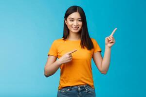 Friendly cheerful asian brunette girl inviting visit link interesting place, pointing upper right corner smiling joyfully camera, telling you about good promotion, stand blue background upbeat photo