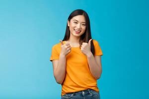 Supportive cute friendly asian girl give thumbs up and smiling, cheering for you, congratulate nice work, approving good idea, like nice outfit, grinning glad accept plan, stand blue background photo